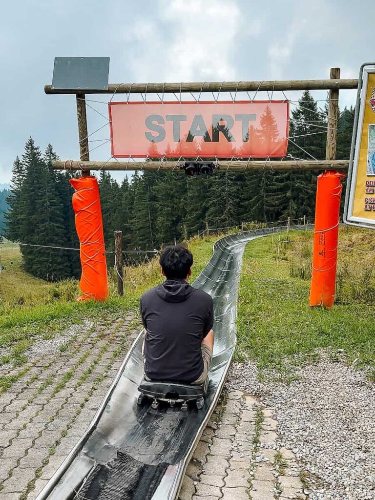 Person sitting at the start of the Pilatus alpine coaster ride in Switzerland surrounded by green hills and forest scenery.